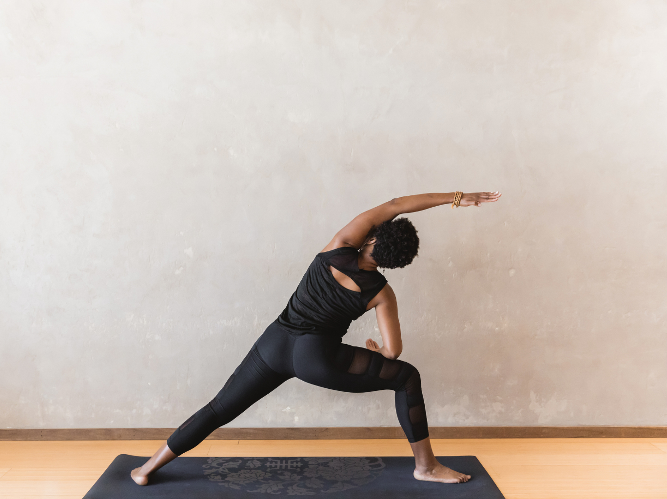 A young Black female entrepreneur at a yoga studio stretching in order to incorporate daily movement into her busy lifestyle.