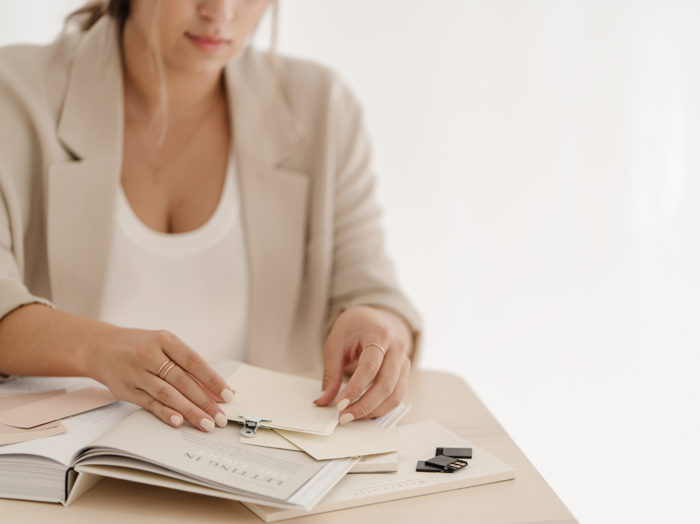 A woman sits at a desk with a planner, an open book, and a collection of notecards spread out in front of her, deliberating the advantages and disadvantages of bootstrapping versus seeking funding for a business venture.