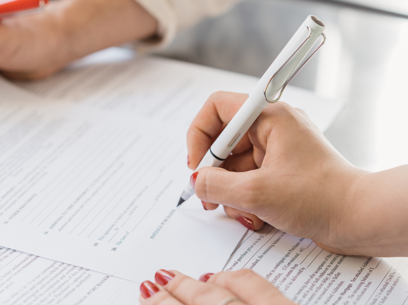 A female entrepreneur holding a pen and adding her signature to the end of a small business legal contract given by her business lawyer.