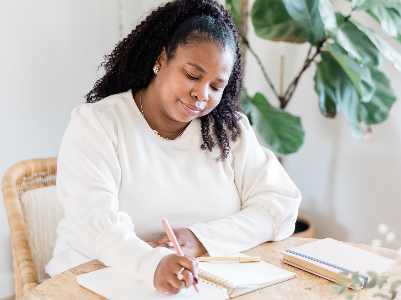 A young African American female entrepreneur sitting at a desk and writing in her notebook while she does her estate planning.